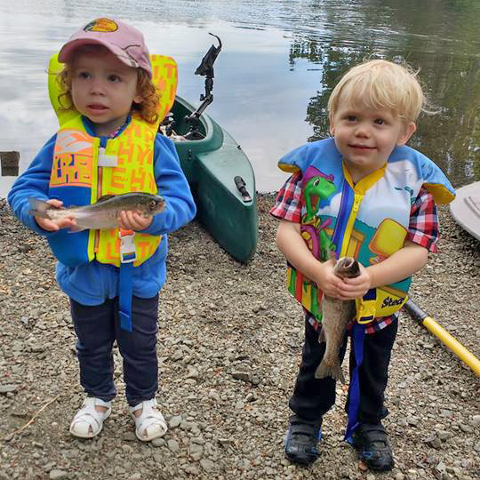 Two kids showing the fish they caught on board the kayak